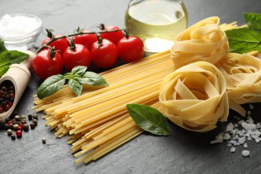 Farklı türde makarna ve malzemeler siyah masada, yakın plan.