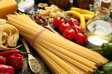 Farklı türde ham makarna, ürünler ve baharatlar siyah ahşap masa üzerinde, yakın plan.