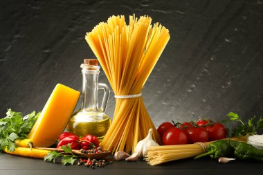 Çiğ spagetti makarna, ürünler ve baharatlar siyah ahşap masa üzerinde koyu dokulu arka plan