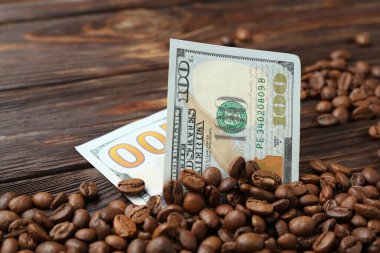 Kavrulmuş kahve çekirdekleri ve katlanmış dolar banknotları ahşap masada, yakın plan.