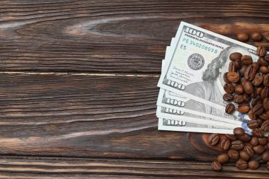 Kavrulmuş kahve çekirdekleri ve dolar banknotları ahşap masada, düz yerde. Metin için boşluk