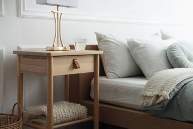 Yatak odasının yanında lamba ve bir bardak su olan komodinin yanında.