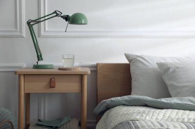 Yatak odasının yanında lamba ve bir bardak su olan komodinin yanında.