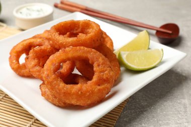 Kızarmış kalamar halkaları, limon, sos ve çubuklar gri masada, yakın plan.