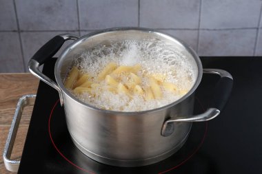 Tencerede taze makarna ve elektrikli ocakta su, yakın plan.