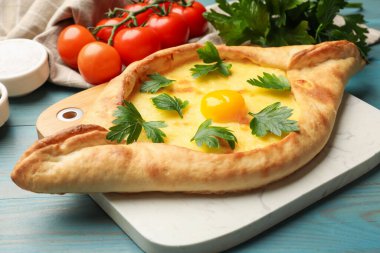 Peynirli, yumurtalı, maydanozlu, domatesli ve baharatlı leziz khachapuri. Açık mavi ahşap masa, yakın plan.