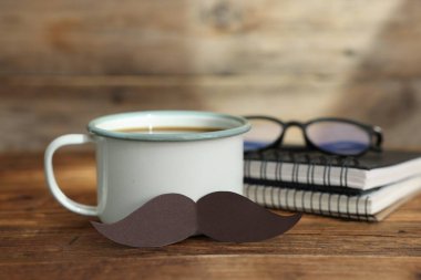 Babalar Günün kutlu olsun. Bıyıklı fincan, defterler ve gözlükler ahşap masada, yakın plan.