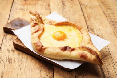 Tahta masadaki peynirli ve yumurtalı lezzetli khachapuri, yakın plan.
