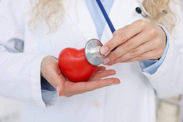 Pediatrician checking heartbeat of heart model in clinic, closeup