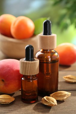 Şişelerdeki, tohumlardaki ve olgun kayısılardaki yağlar ahşap masada bulanık yeşil arka planda, yakın planda.