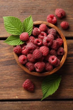 Taze olgun ahududular kasede ve yeşil yapraklar ahşap masada, düz yatıyordu.