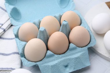 Yumurta kartonunda çiğ tavuk yumurtası, beyaz fayanslı masa, yakın plan.