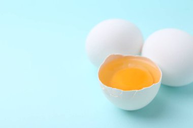 Açık mavi arka planda bütün ve kırılmış tavuk yumurtaları, yakın plan. Metin için boşluk