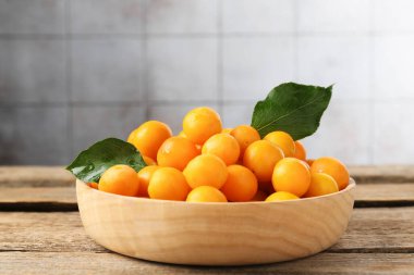 Olgun sarı kiraz erikleri ve yapraklar ahşap masada, yakın plan.