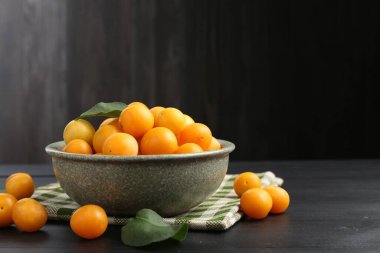 Siyah ahşap masanın üzerinde yaprakları olan olgun sarı kiraz erikleri. Metin için boşluk