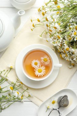 Lezzetli papatya çayı, zerk makinesi ve çiçekler beyaz ahşap masada, düz uzanmış.