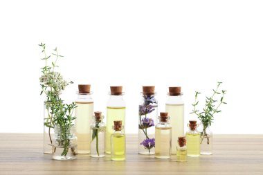 Beyaz arka plana karşı ahşap masa üzerinde gerekli yağlar ve farklı otlar.