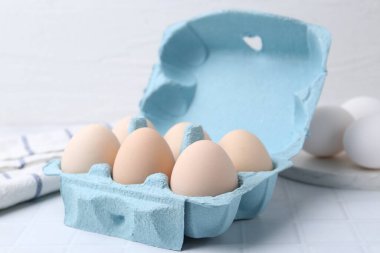 Yumurta kartonunda çiğ tavuk yumurtası, beyaz fayanslı masa, yakın plan.