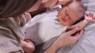 Anne, uyuyan yeni doğmuş bebeğiyle evde, yatakta, yakın plan.