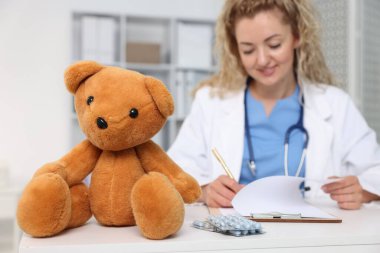 Hastanede masa başında çalışan çocuk doktoru ve oyuncak ayı, seçici odaklanma