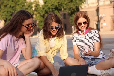 Üç arkadaş dışarıda dizüstü bilgisayardan bir şey izliyor.