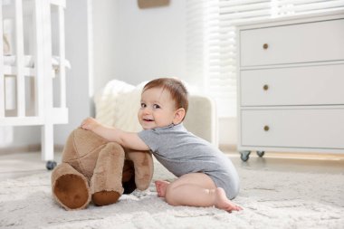 Küçük şirin bebek odada oyuncak ayıyla oynuyor.