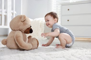 Küçük şirin bebek odada oyuncak ayıyla oynuyor.