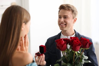 Nişan yüzüğüyle ve gül buketiyle gülümseyen bir adam kız arkadaşına evlenme teklif ediyor.