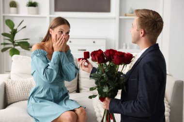 Nişan yüzüğü ve gül buketi takmış bir adam heyecanlı sevgilisine evde evlenme teklif ediyor.