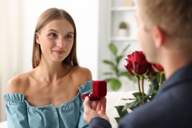 Nişan yüzüğü ve gül buketi takmış bir adam kız arkadaşına evlenme teklif ediyor.