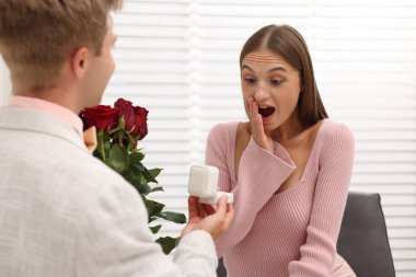 Nişan yüzüğü ve gül buketi olan bir adam evde duygusal kız arkadaşına evlenme teklif ediyor.