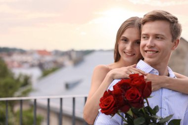 Evlilik teklifi. Nişan yüzüğüyle gülümseyen kadın ve nişanlısı balkonda gül buketi tutuyor. Metin için boşluk