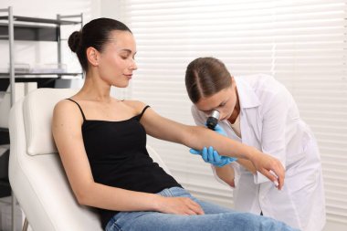 Doktor hastanede dermatoskopla genç kadının benini inceliyor.