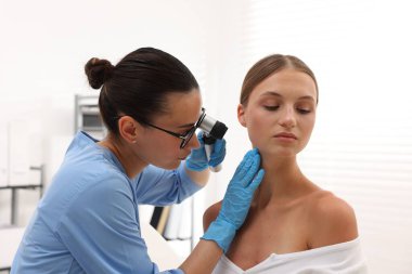 Doktor hastanede dermatoskopla genç kadının benini inceliyor.