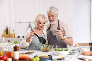 Yaşlı çift mutfaktaki masada birlikte yemek pişiriyor.
