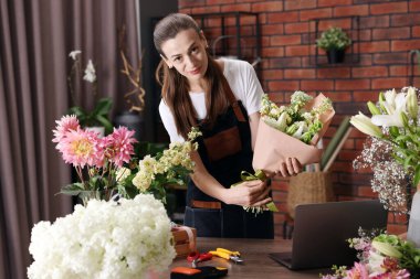 Profesyonel çiçekçi dükkandaki ahşap masada çiçek buketi yapıyor.