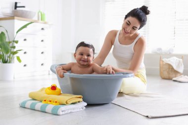 Anne küçük bebeğini evde yıkıyor.