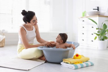 Anne küçük bebeğini evde yıkıyor.