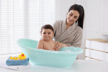 Annesi küçük bebeğini evde yıkıyor.