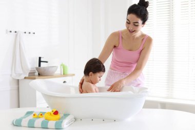 Anne küçük bebeğini evde yıkıyor.