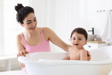 Anne küçük bebeğini evde yıkıyor.