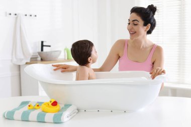 Anne küçük bebeğini evde yıkıyor.