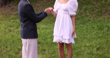 Evlilik teklifi yapıyor. Erkek, kız arkadaşının parmağına nişan yüzüğü takıyor. Kamera yukarı ve sola hareket ediyor.