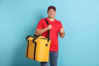 Termo çantalı kurye açık mavi arka planda baş parmak gösteriyor. Yemek dağıtım servisi.