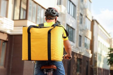 Termo çantalı bir kurye dışarıda bisiklet sürüyor, arkadan bakıyor. Yemek dağıtım servisi.