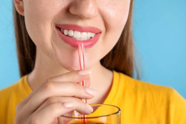 Açık mavi arka planda samandan meyve suyu içen kadın, yakın plan.