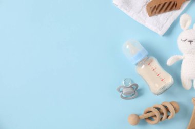 Açık mavi zemin üzerinde süt ve bebek aksesuarları olan bir şişe. Metin için boşluk