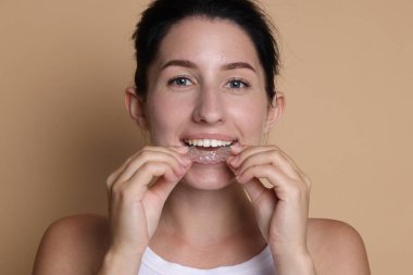 Bej arka planda diş hizası takan genç bir kadın.