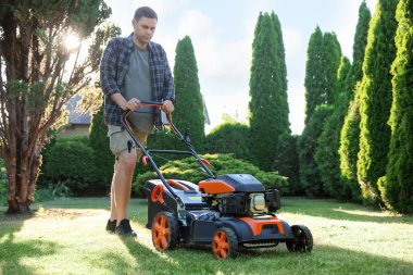 Bahçede çim biçme makinesiyle yeşil çim biçen bir adam