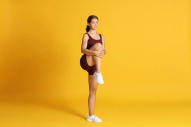 Spor giyimli genç kız turuncu arka planda geriniyor.